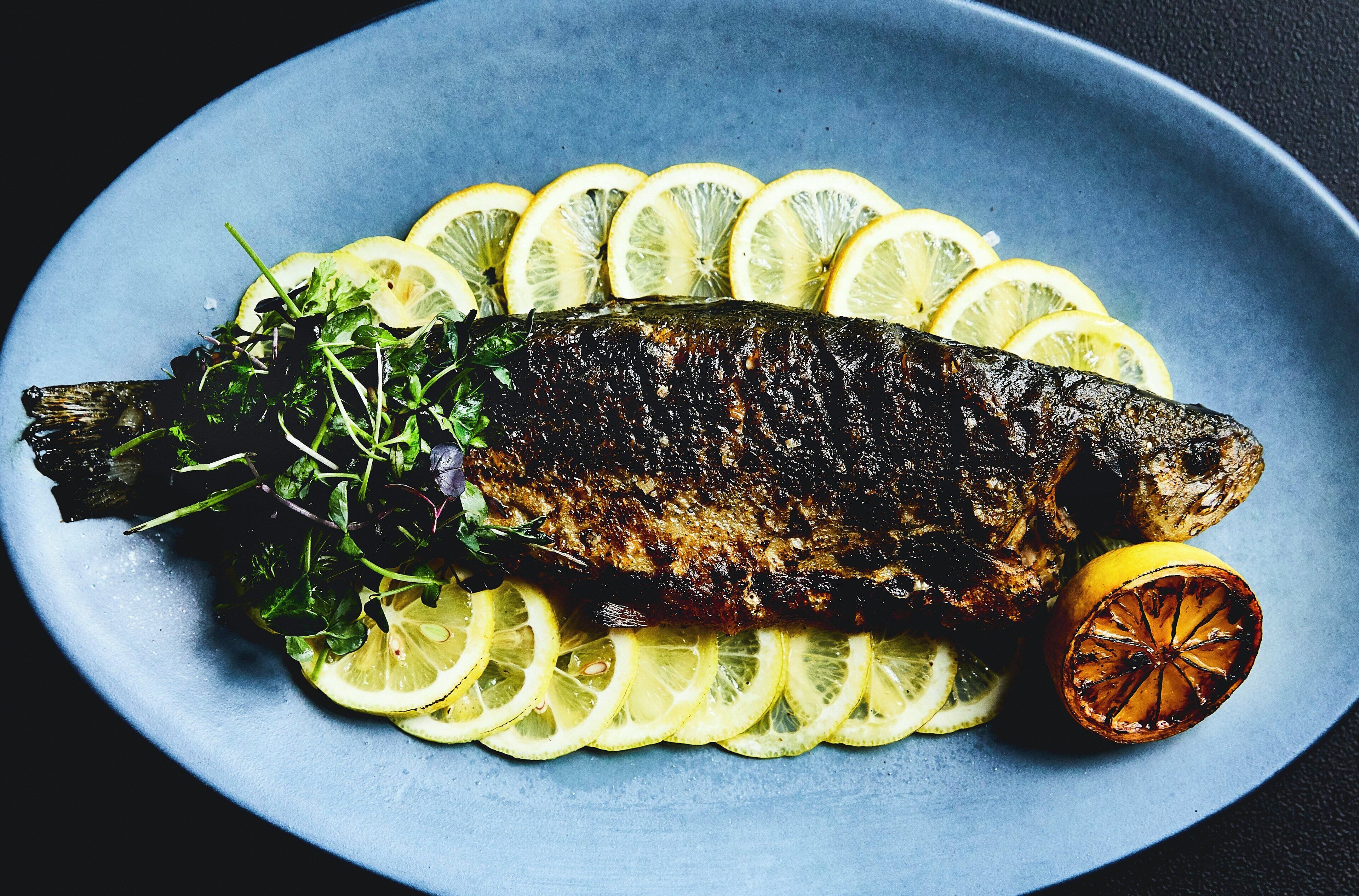 A grilled fish on a plate with lemon slices and greens.