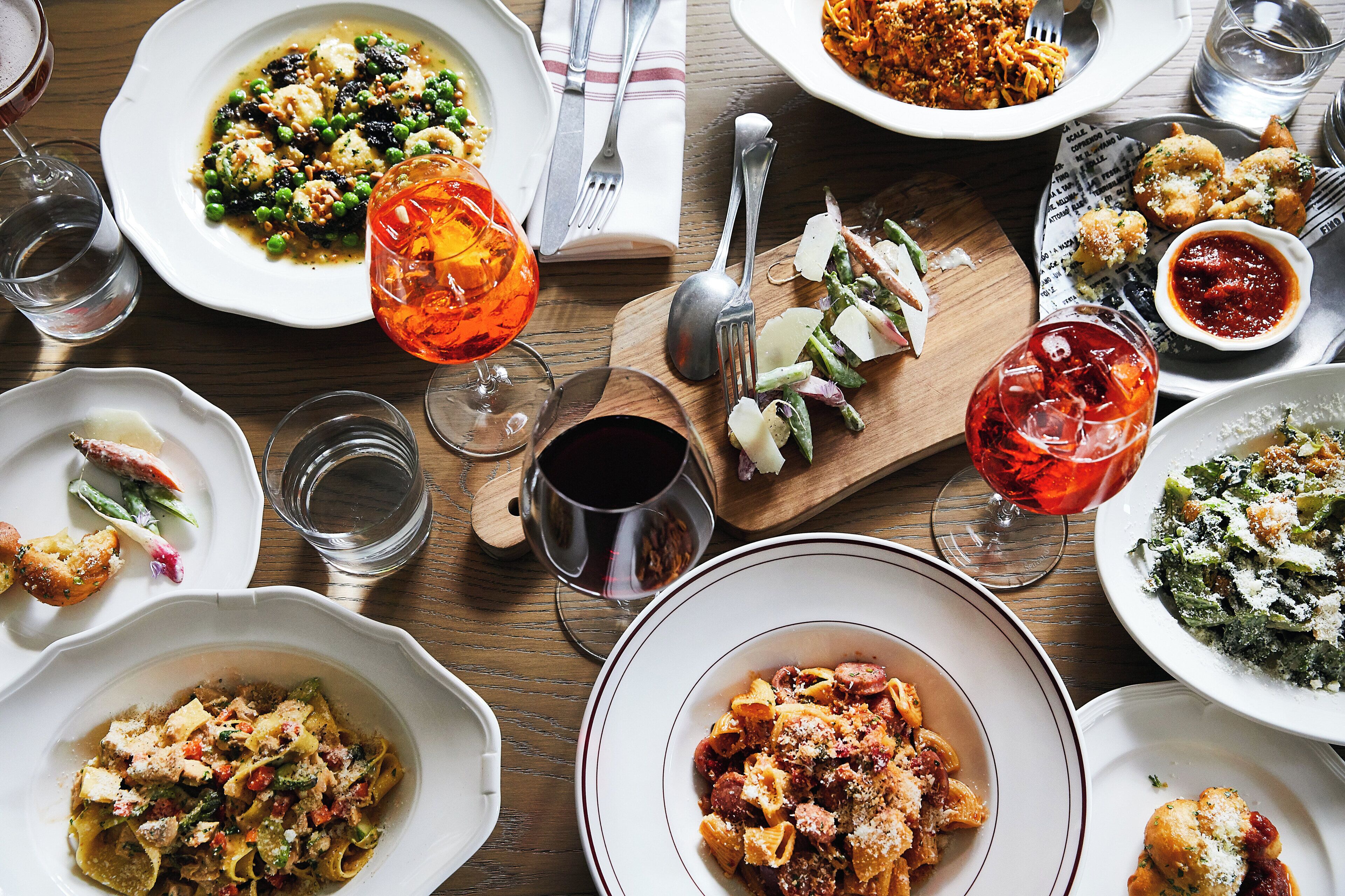 A variety of dishes on a wooden table, including pasta, vegetables, and a glass of red wine.