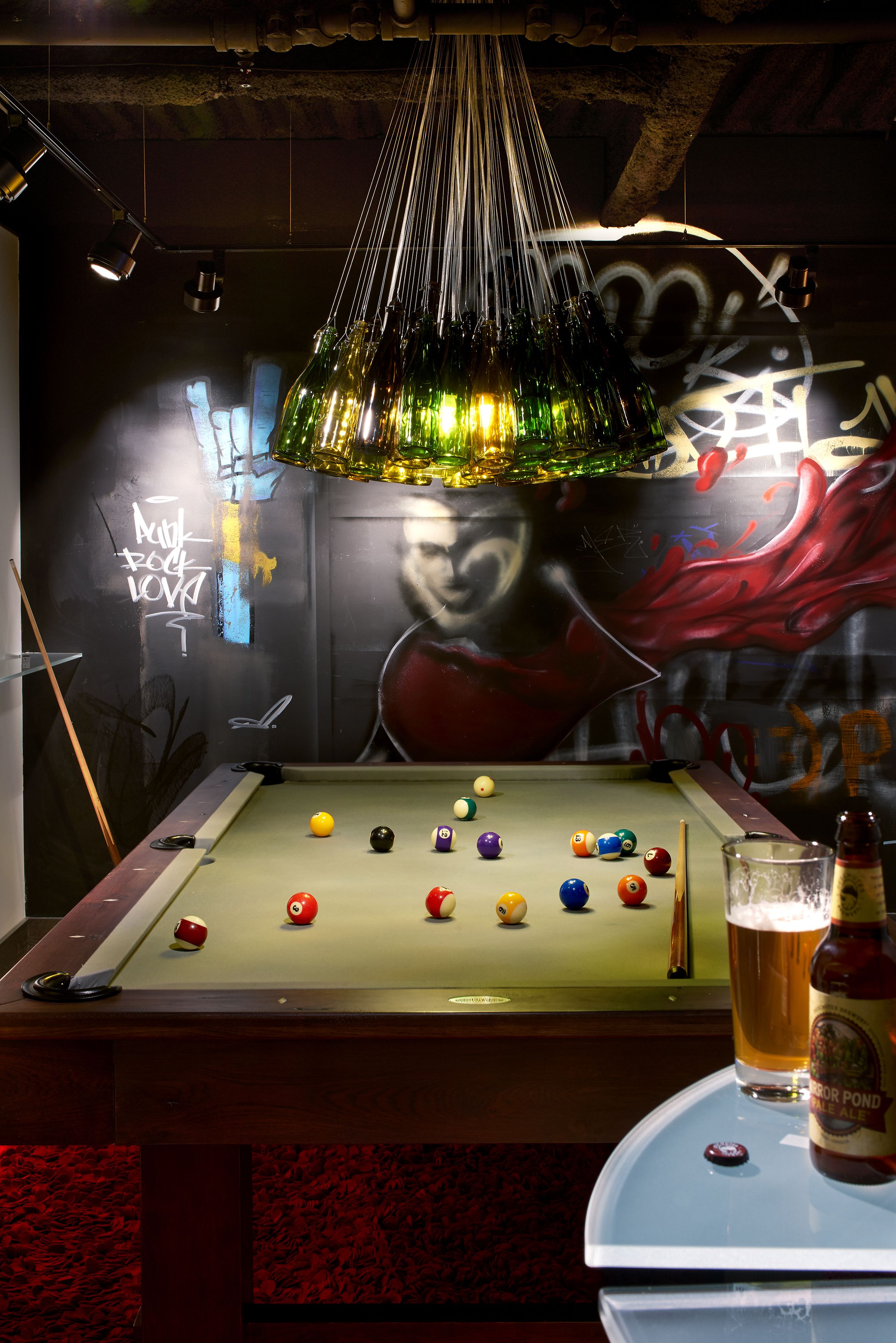 Una mesa de billar con bolas de varios colores, una cerveza en un vaso y una botella sobre la mesa.