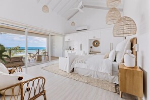 Un dormitorio con una cama grande, una mesita de noche de madera y vista al océano.