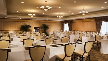 Une salle de banquet avec de nombreuses tables rondes, chacune étant agrémentée de chaises, de bouteilles d’eau et de verres.