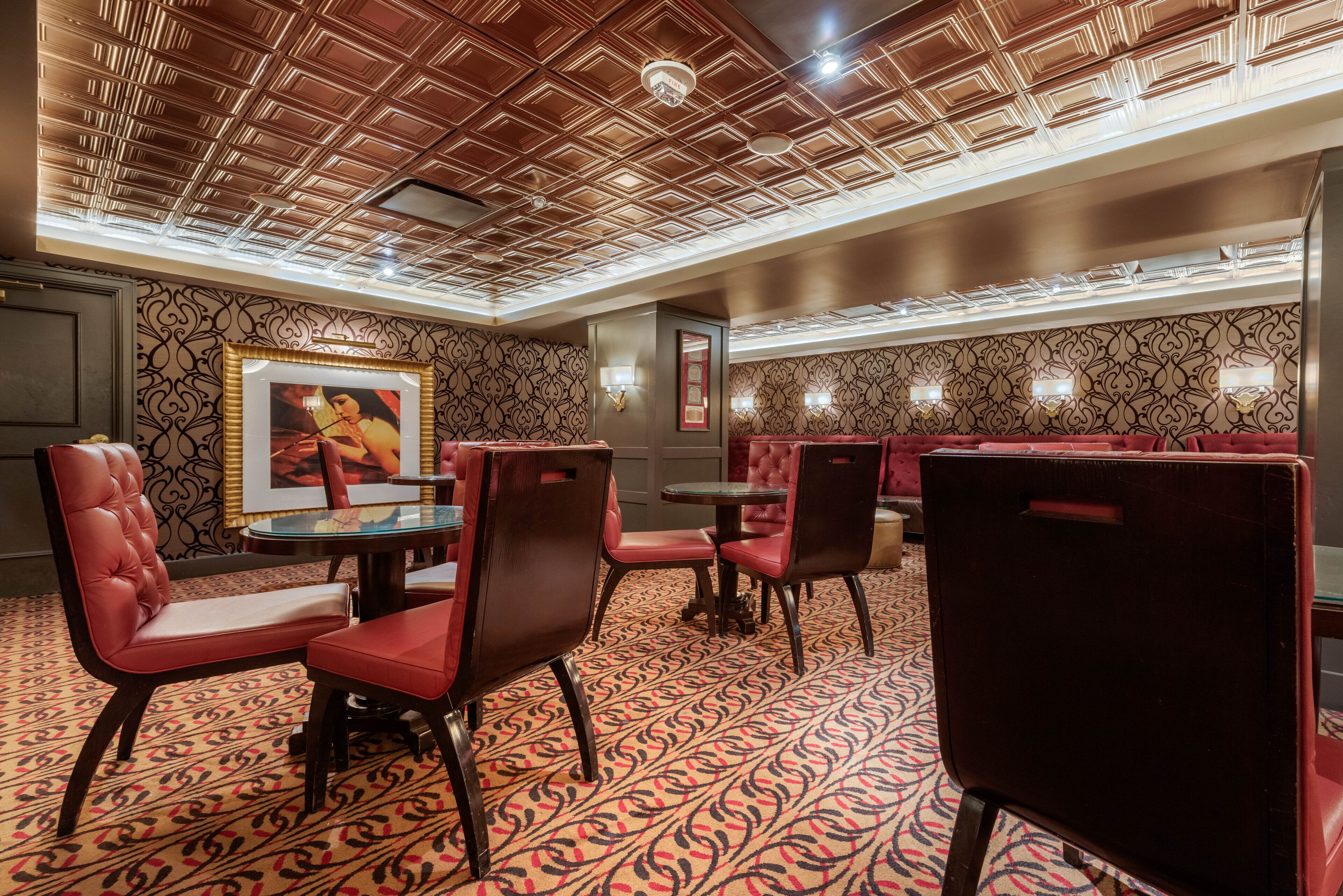 A restaurant with red upholstered booths and chairs, patterned carpet, and a wooden ceiling with recessed lighting.