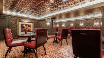 A restaurant with red upholstered booths and chairs, patterned carpet, and a wooden ceiling with recessed lighting.