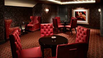 A room with red upholstered chairs and a round table, patterned carpet, and a framed picture on the wall.