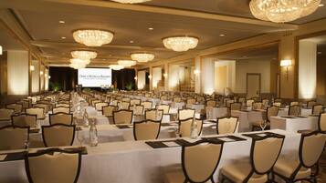 A banquet hall with rows of tables, chairs, and chandeliers.