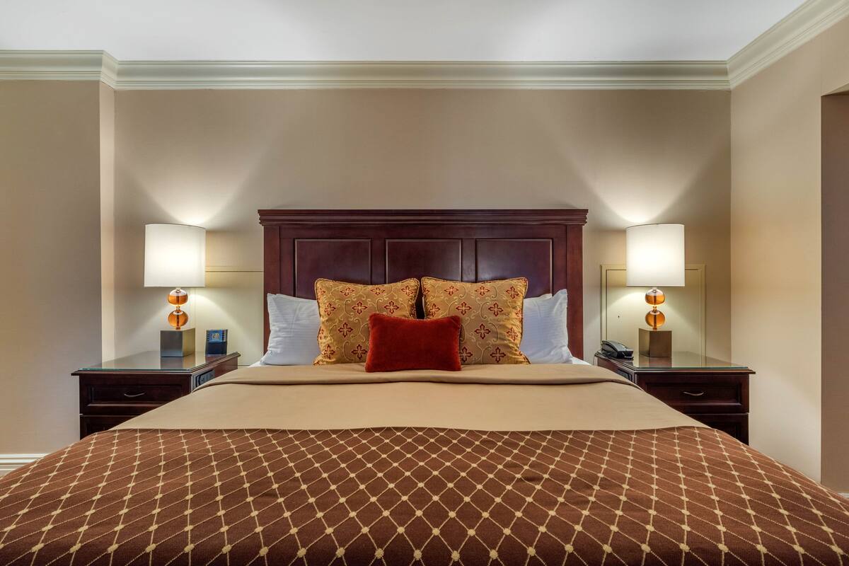 A neatly made bed with a patterned bedspread, a wooden headboard, and two bedside lamps.
