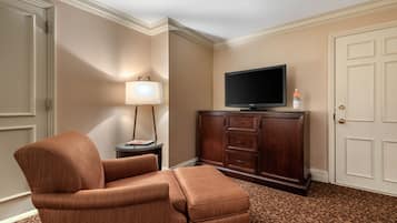A hotel room with a brown upholstered armchair, a television on a wooden cabinet, a lamp, and a patterned carpet.