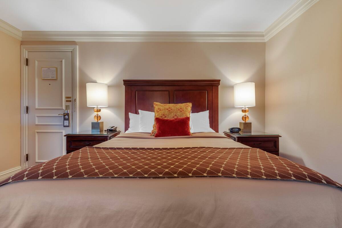 A neatly made bed with a patterned bedspread, two bedside lamps, and a wooden headboard.