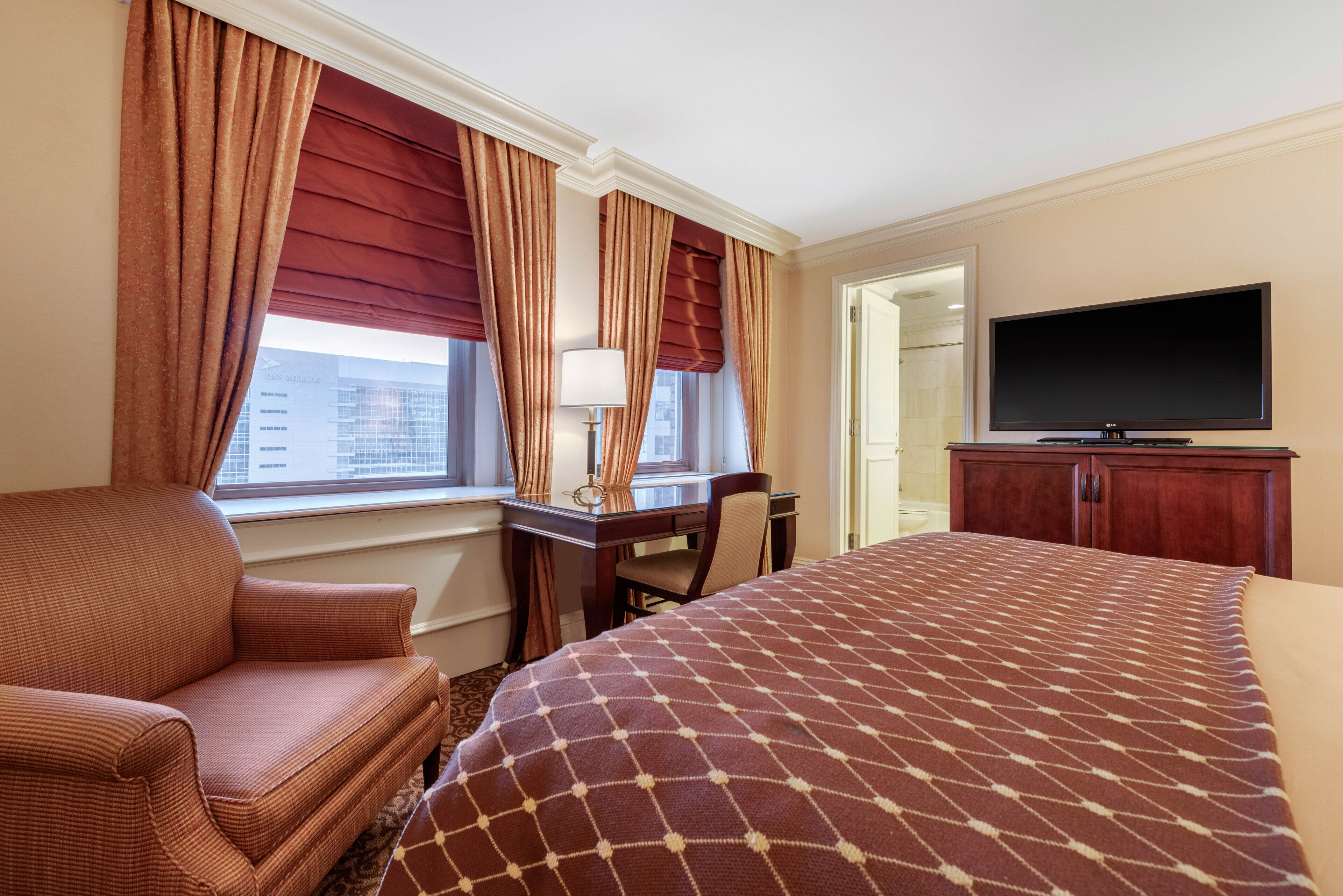 Une chambre d’hôtel équipée d’un lit, d’un bureau, d’une chaise, d’une télévision et d’une fenêtre avec des rideaux.