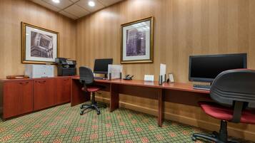 A conference room with two desks, chairs, a filing cabinet, and framed pictures on the walls.