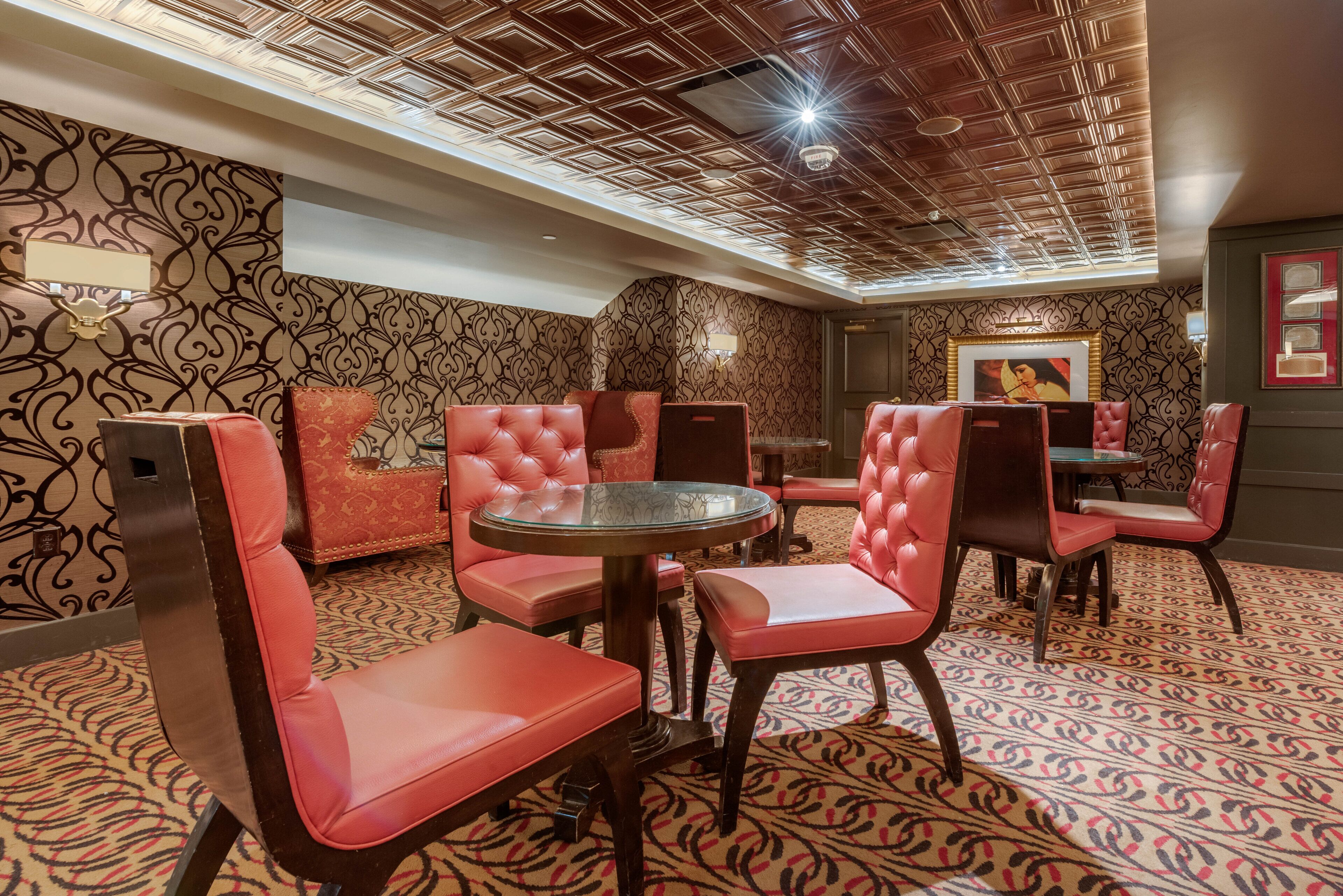 A room with patterned wallpaper, red upholstered chairs, a round glass table, and a ceiling with a geometric design.