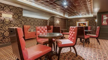 A room with patterned wallpaper, red upholstered chairs, a round glass table, and a ceiling with a geometric design.