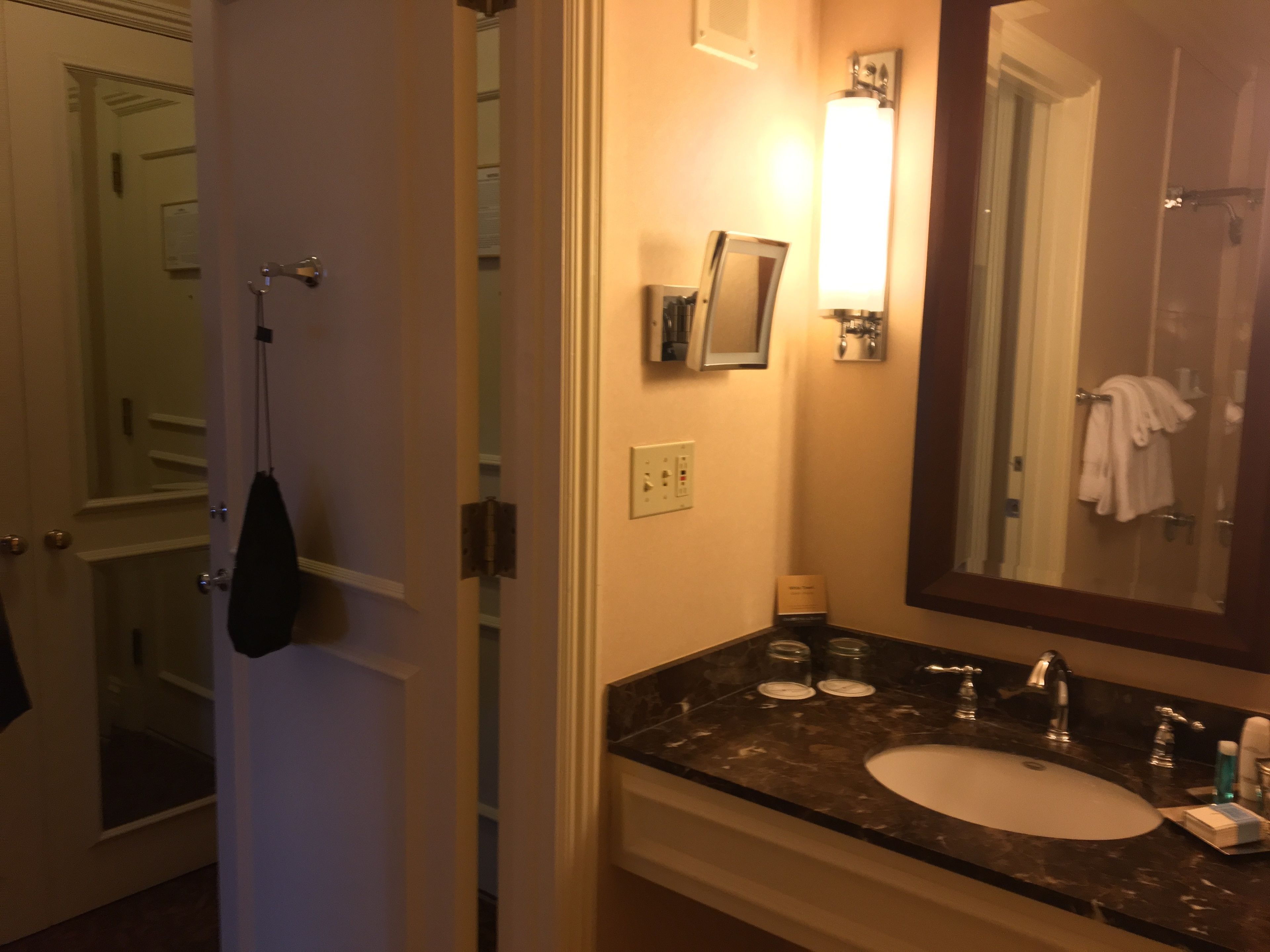 A bathroom with a sink, mirror, towel rack, and a door leading to another room.