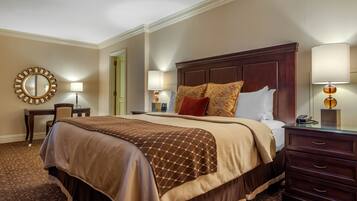 A hotel room with a large bed, a wooden headboard, a desk with a chair, two bedside lamps, and a mirror on the wall.