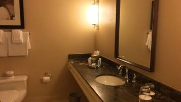 A bathroom with a toilet, sink, mirror, and a trash can.