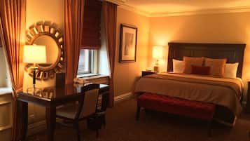 A hotel room with a bed, bedside table, lamp, desk, chair, and a large mirror.