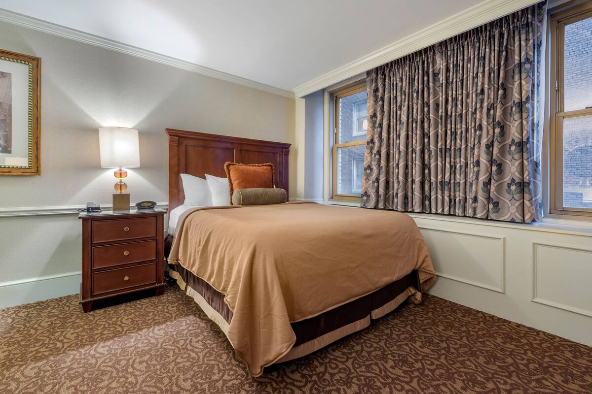 A hotel room with a bed, a nightstand, a lamp, and a window with curtains.