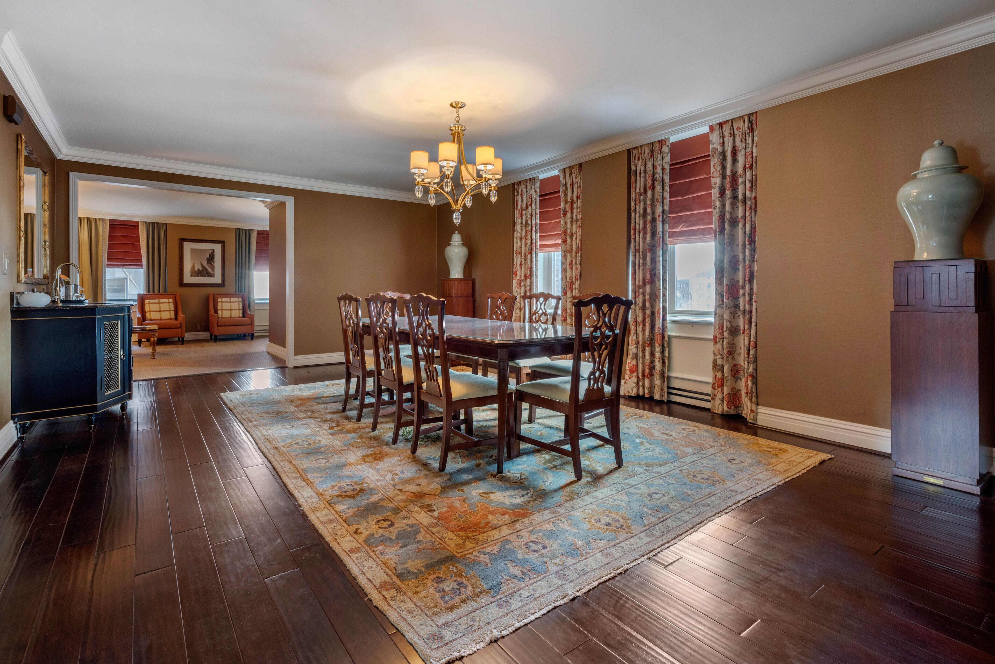 A dining room with a wooden table and chairs, a chandelier, and a patterned rug.