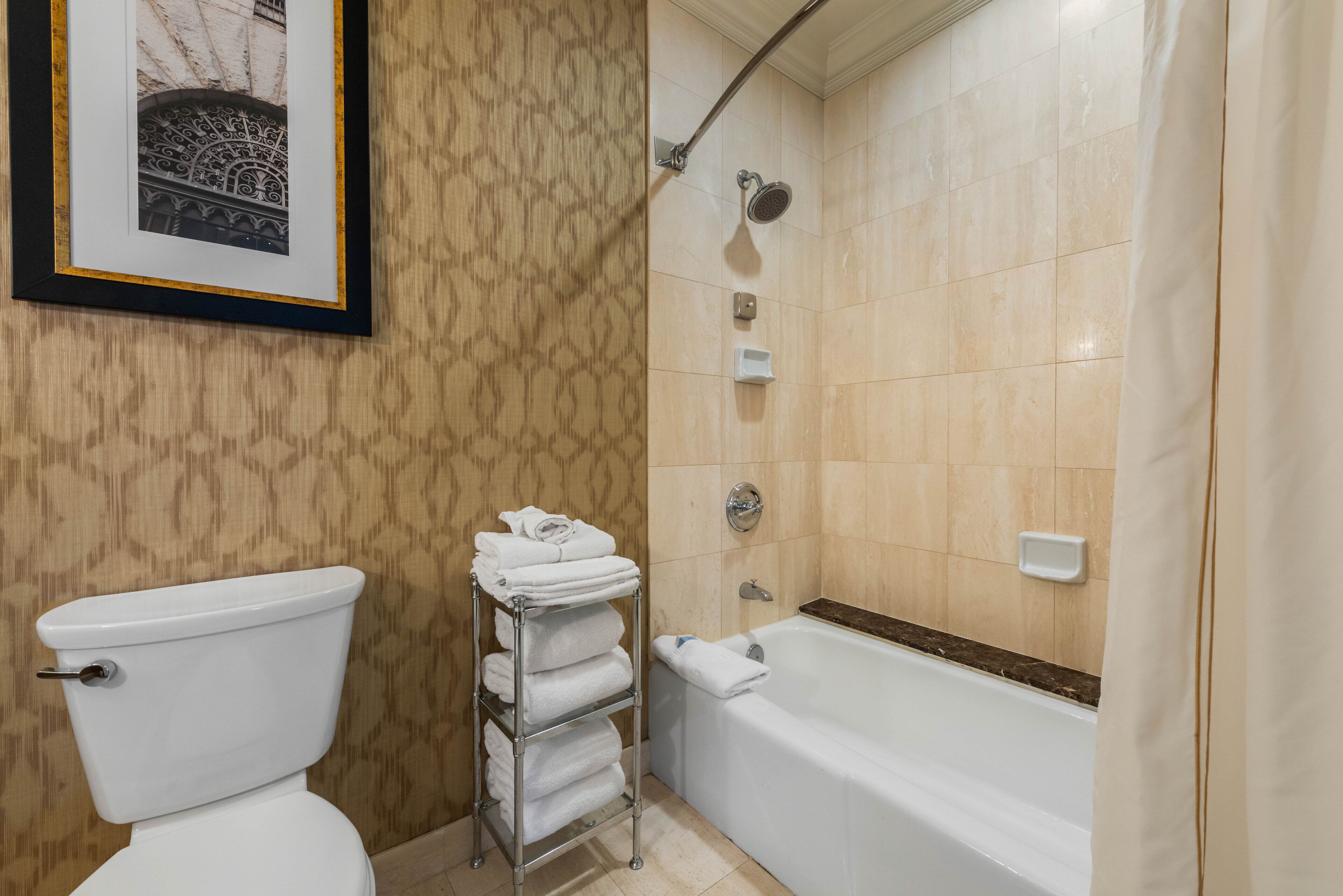 A bathroom with a toilet, a towel rack with folded towels, a shower with a handheld showerhead, and a bathtub.