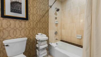 A bathroom with a toilet, a towel rack with folded towels, a shower with a handheld showerhead, and a bathtub.