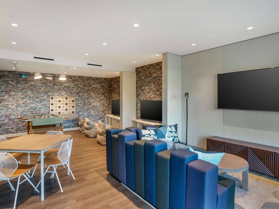 A modern living room with a wooden table, white chairs, a sofa, and a TV mounted on the wall.