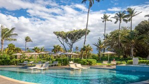 A swimming pool with lounge chairs and umbrellas, surrounded by palm trees and greenery.