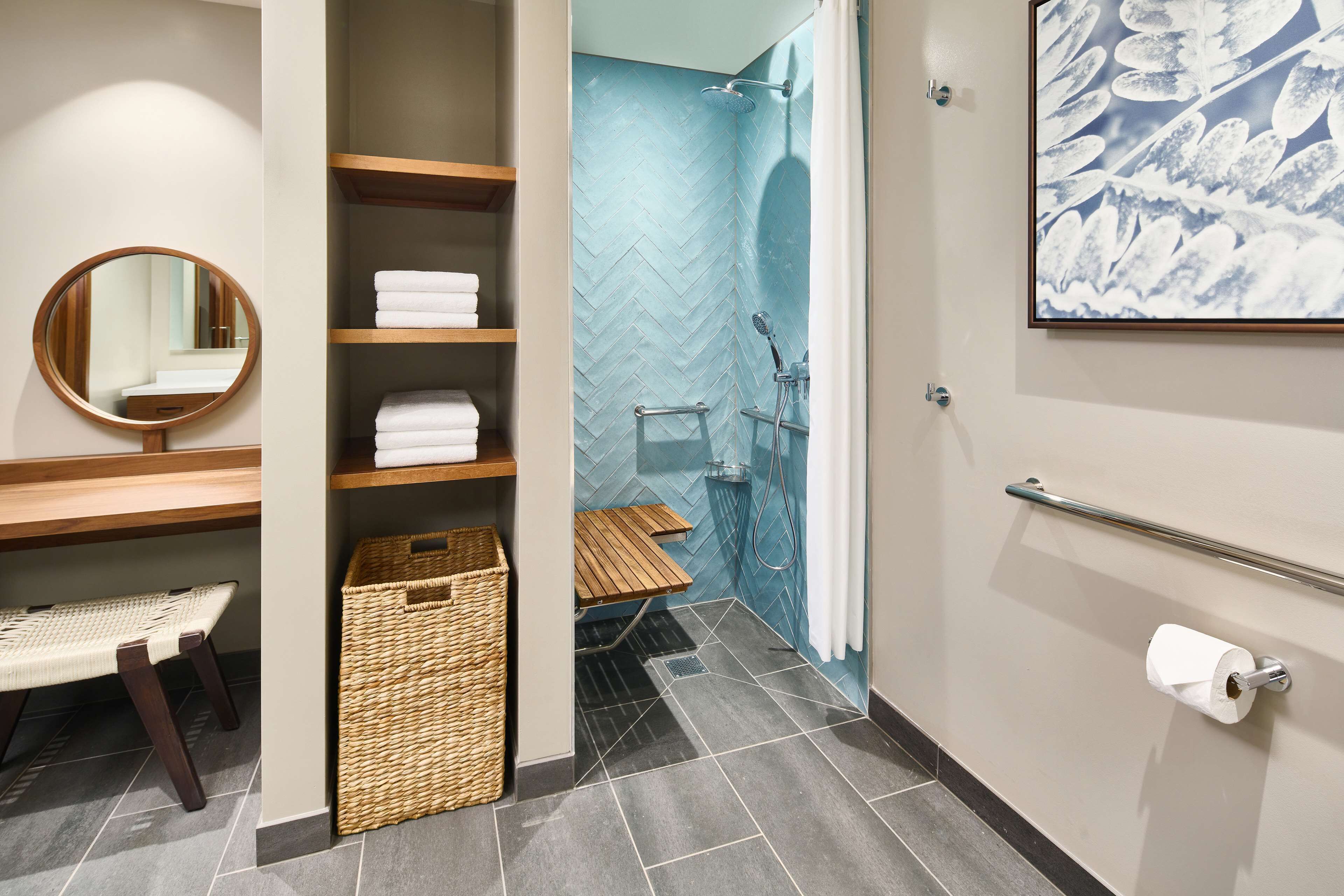 A modern bathroom with a shower, a round mirror, shelves with towels, and a wicker basket.