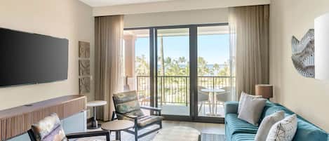 A hotel room with a large balcony, a sofa, a chair, a coffee table, and a TV.