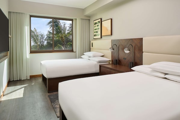 Une chambre d’hôtel avec deux lits, une grande fenêtre avec des rideaux, un téléviseur à écran plat et une tête de lit en bois.