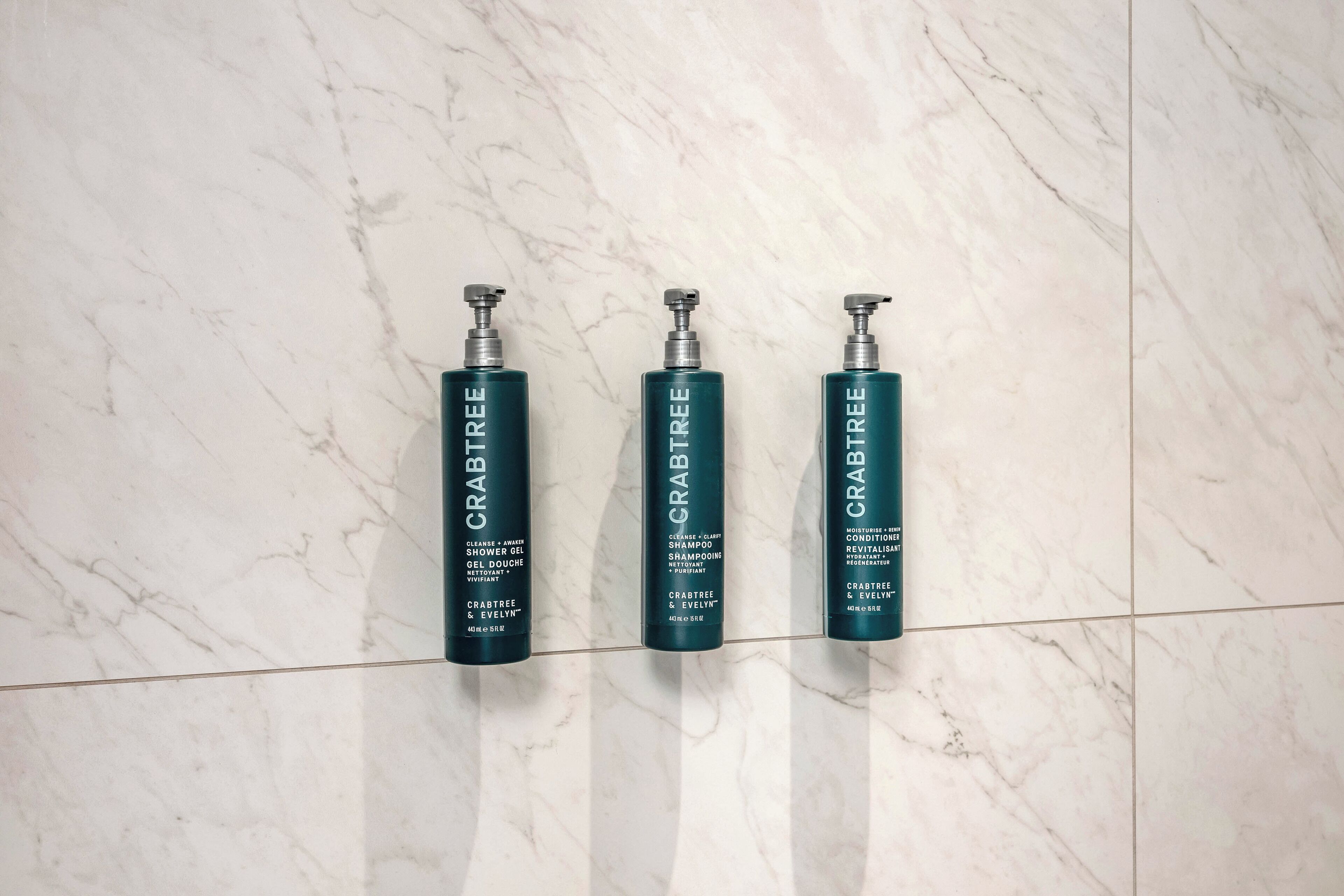 Three bottles of Crabtree shampoo and conditioner on a marble floor.