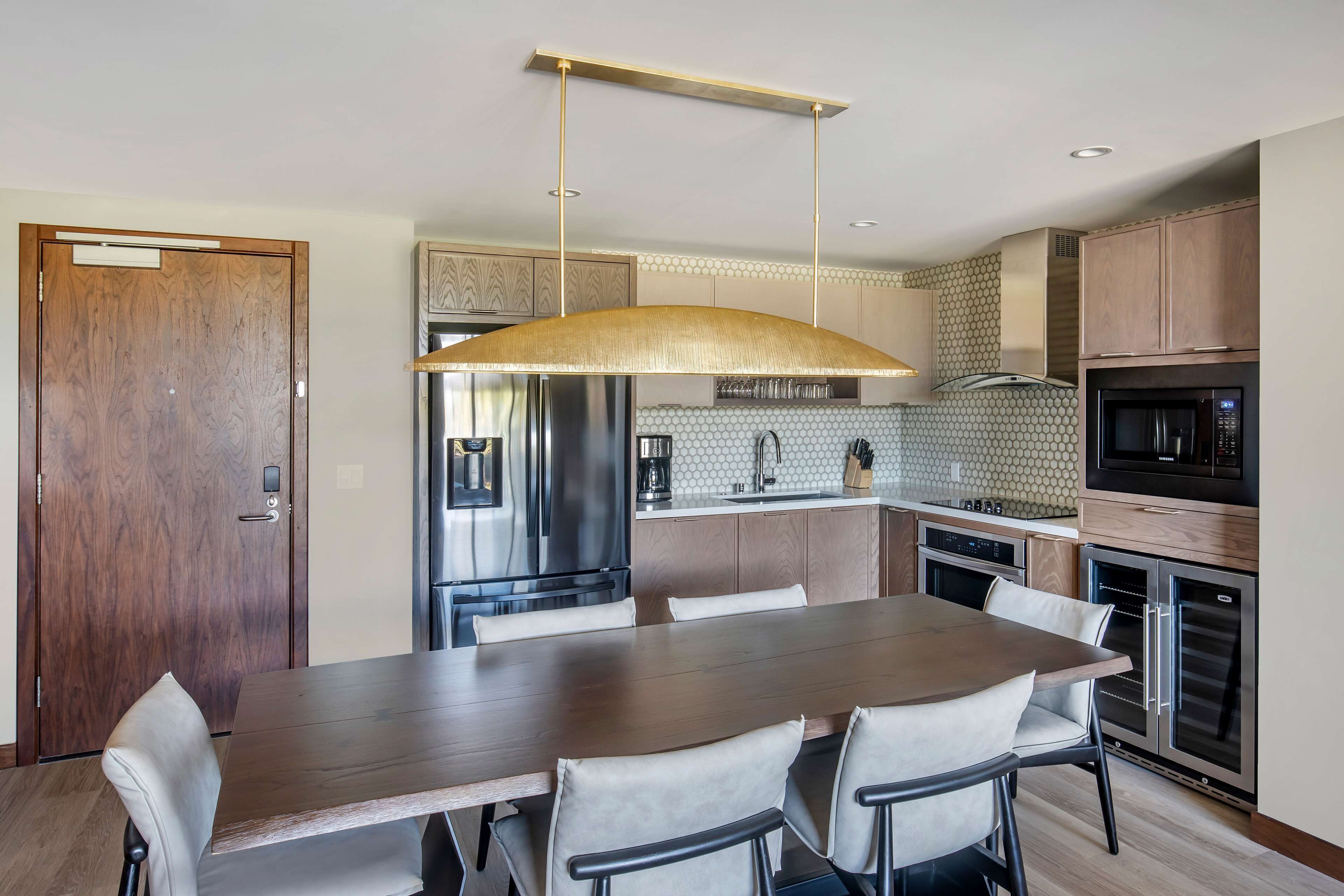 A modern kitchen with a wooden dining table, chairs, and stainless steel appliances.