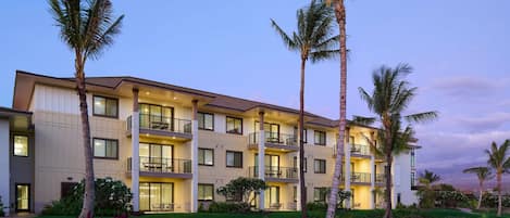 A multi-story hotel with balconies, a well-maintained lawn, and palm trees.