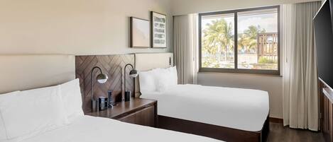 A hotel room with two beds, a large window with a view of palm trees, and a flat-screen TV.