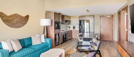 Una sala de estar moderna con un sofá color turquesa, un comedor con mesa de madera y una cocina con electrodomésticos de acero inoxidable.