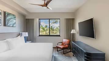 A hotel room with a bed, a desk, a chair, a television, and a window with a view of palm trees.