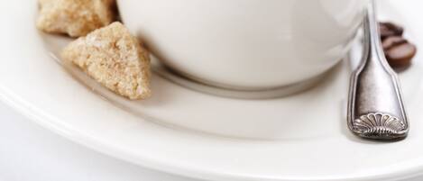 A white cup of coffee on a saucer with a spoon, accompanied by a bowl of fruit and a croissant.