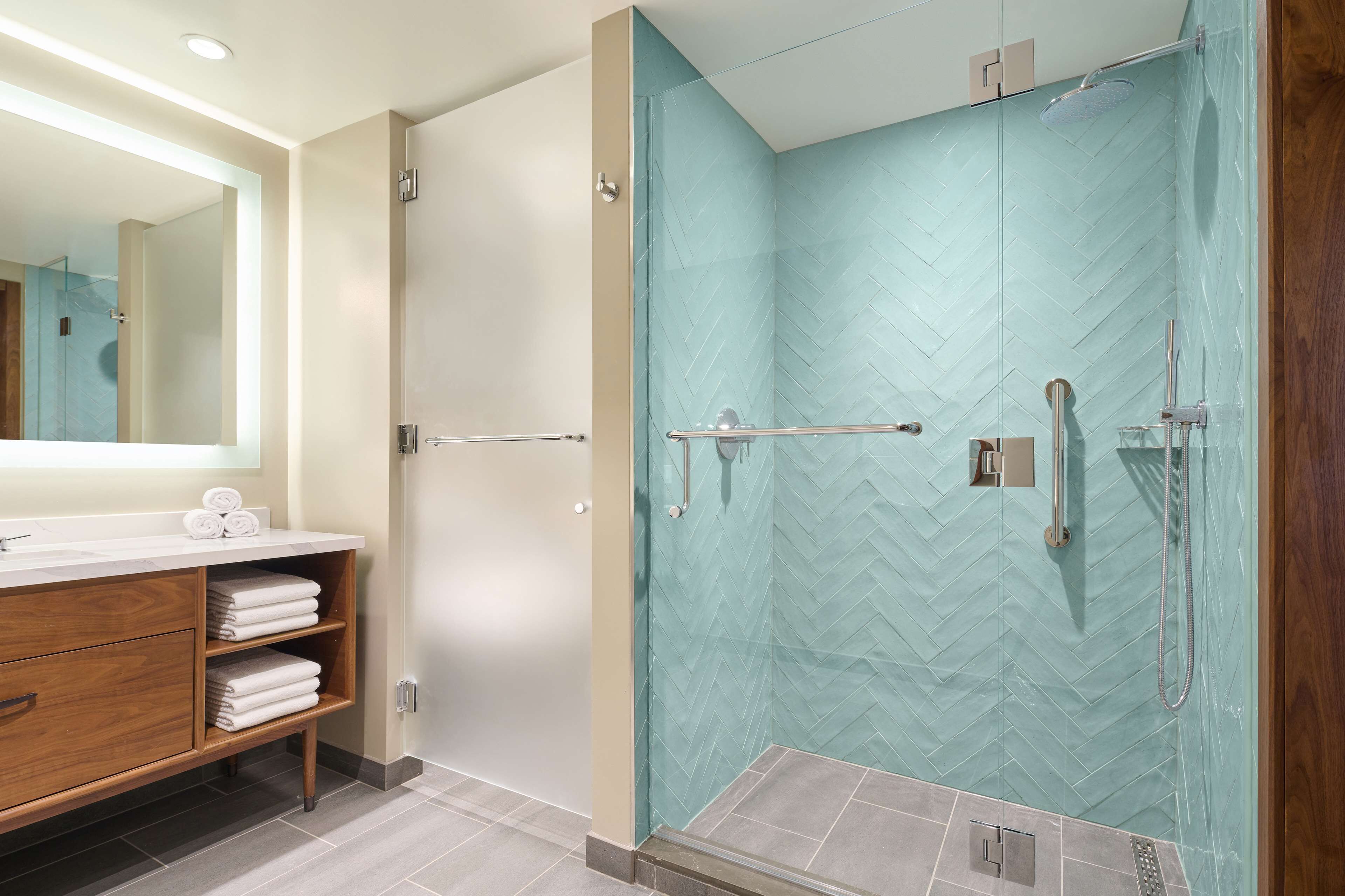 A modern bathroom with a glass-enclosed shower, a wooden vanity with a mirror, and neatly folded towels.