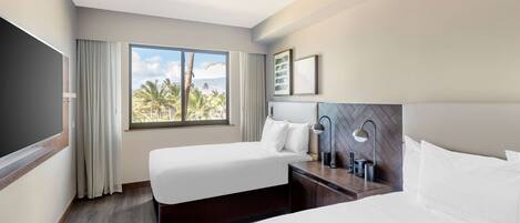 A hotel room with two beds, a ceiling fan, a large window with curtains, a flat-screen TV, and a nightstand with a lamp.