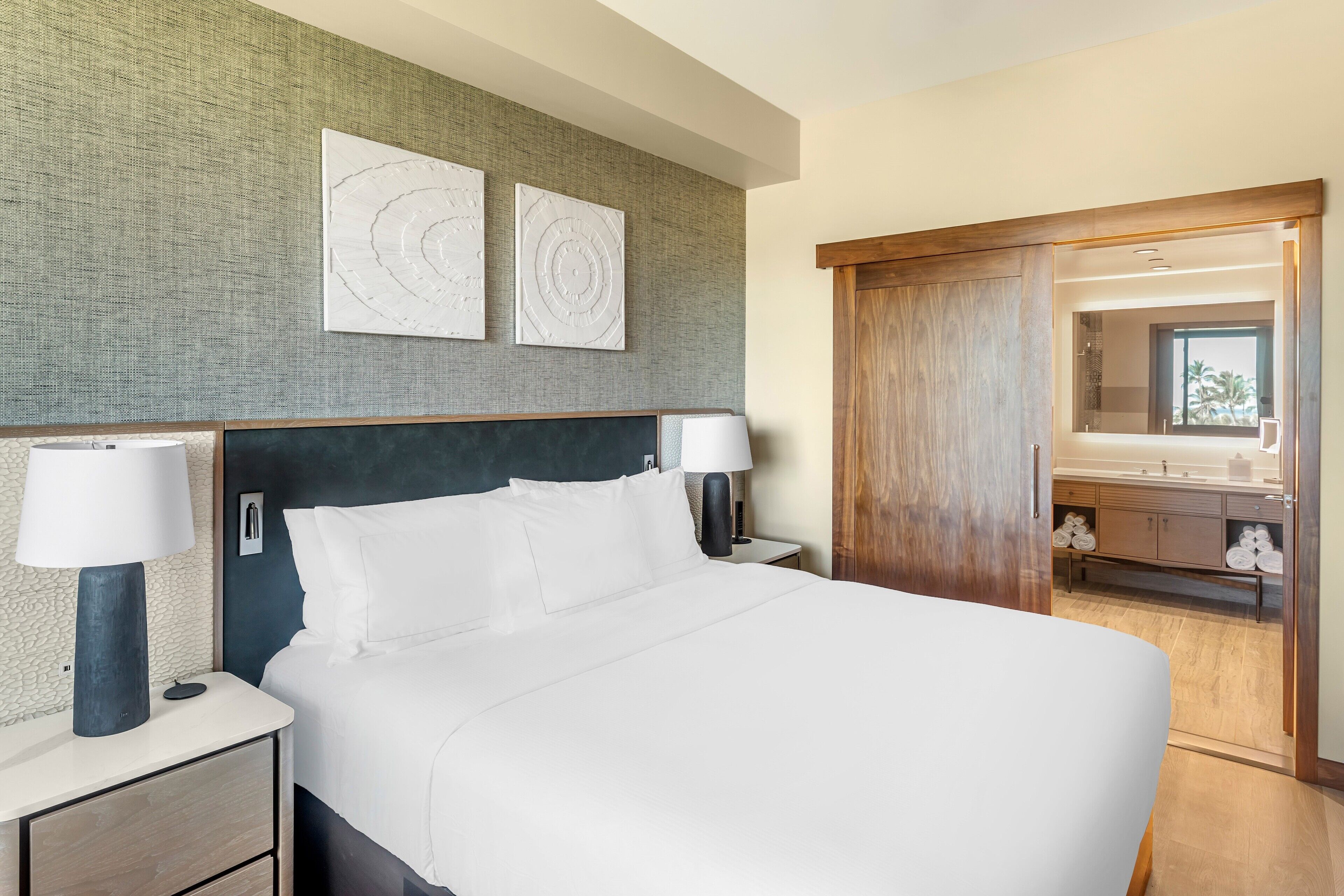 Een hotelkamer met een groot bed, twee nachtkastjes met lampen, een houten garderobe en een spiegel.