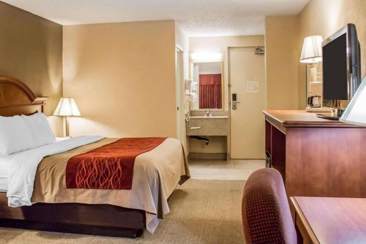 A hotel room with a bed, a desk, a television, and a bathroom visible through an open door.