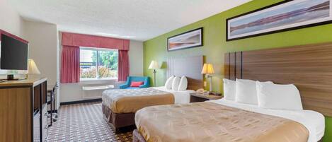 Habitación de hotel con dos camas, un escritorio, un televisor y una ventana con cortinas.