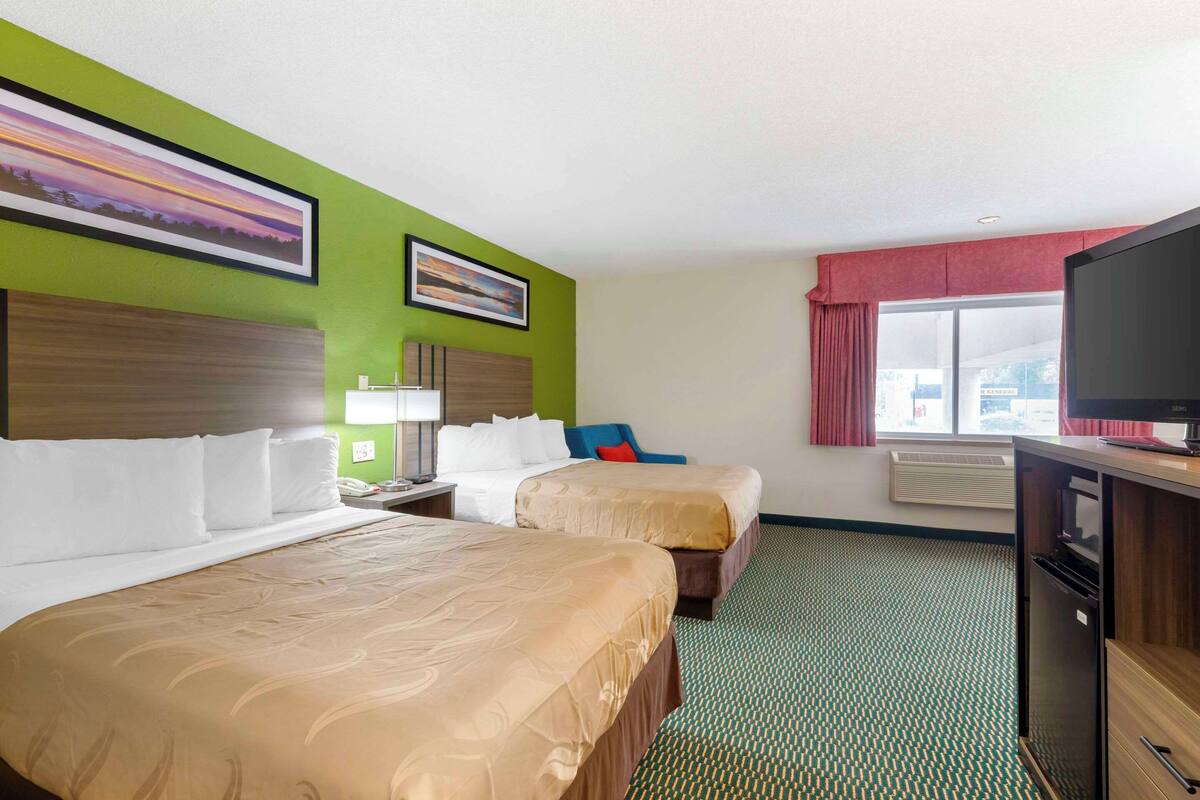A hotel room with two beds, a television, a desk, and a window with curtains.
