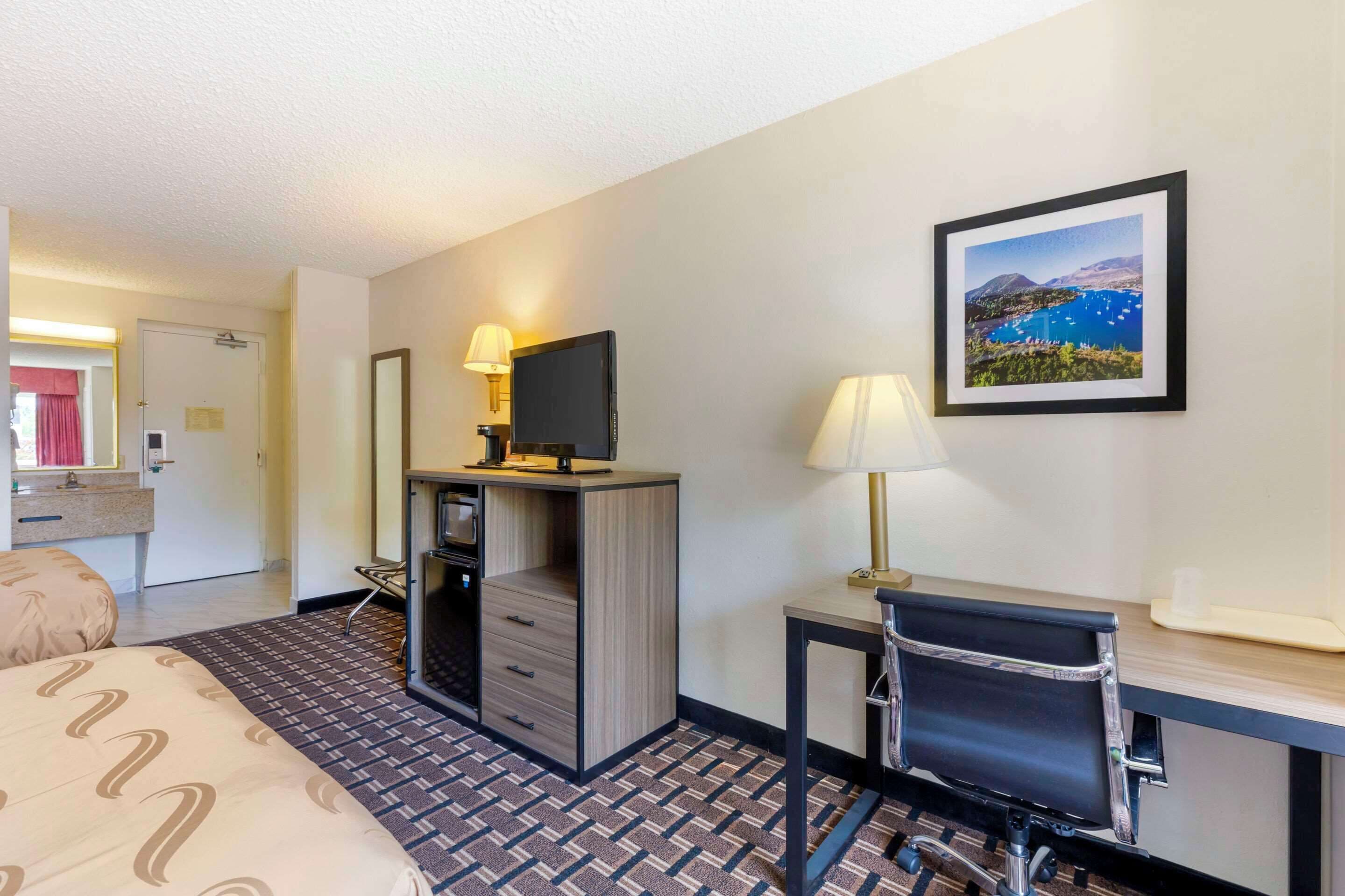 A hotel room with a bed, desk, chair, TV, and a framed picture on the wall.