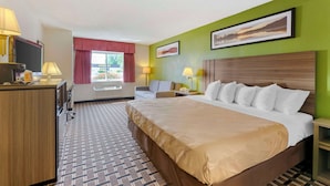 Una habitación de hotel con una cama grande, un escritorio con televisor, una silla y una ventana con cortinas rojas.