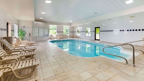 Una piscina interior con sillas de descanso y suelo de baldosas.