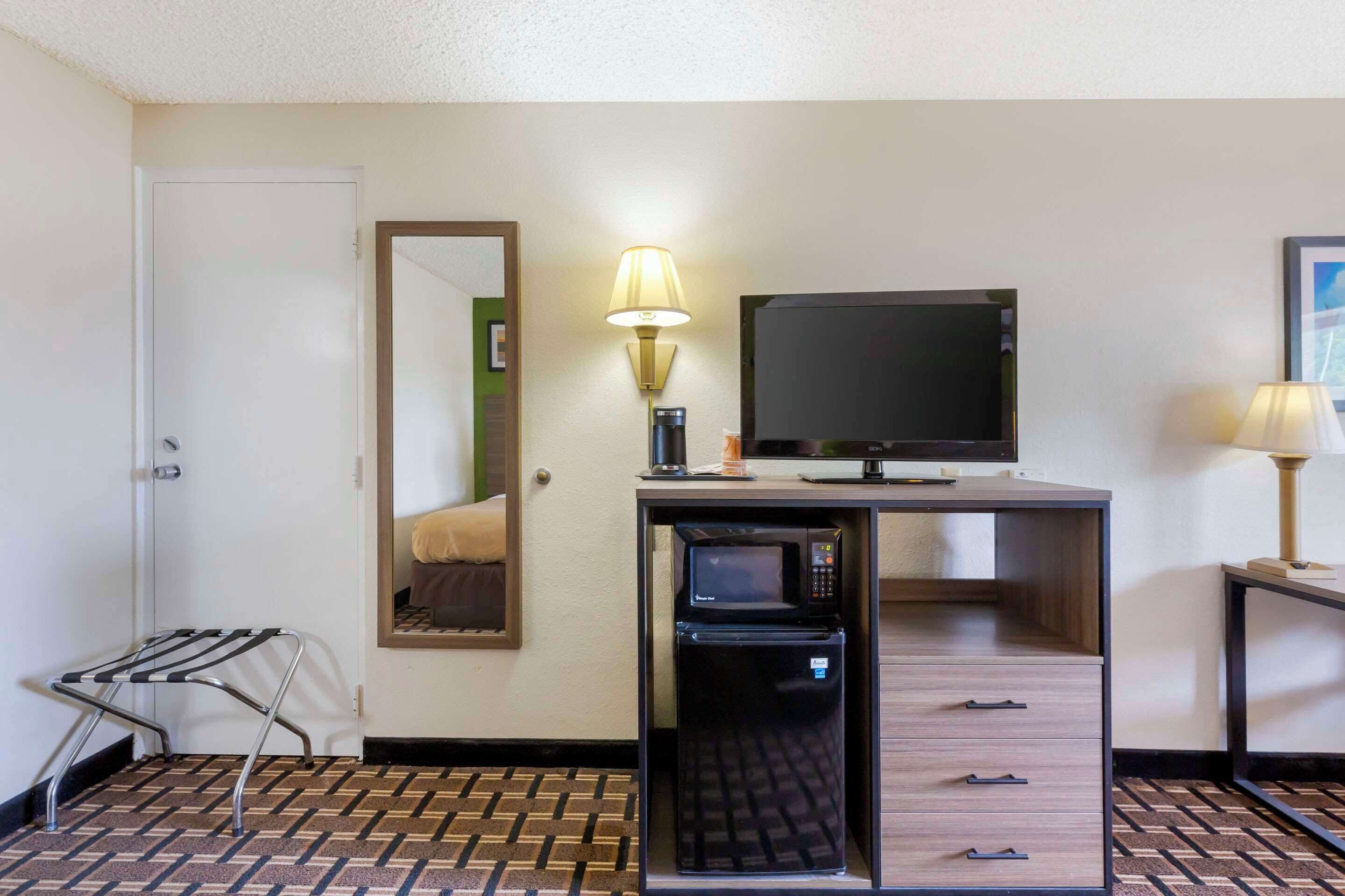 Una habitación de hotel compacta con kitchenette, televisor de pantalla plana, refrigerador pequeño y un espejo.