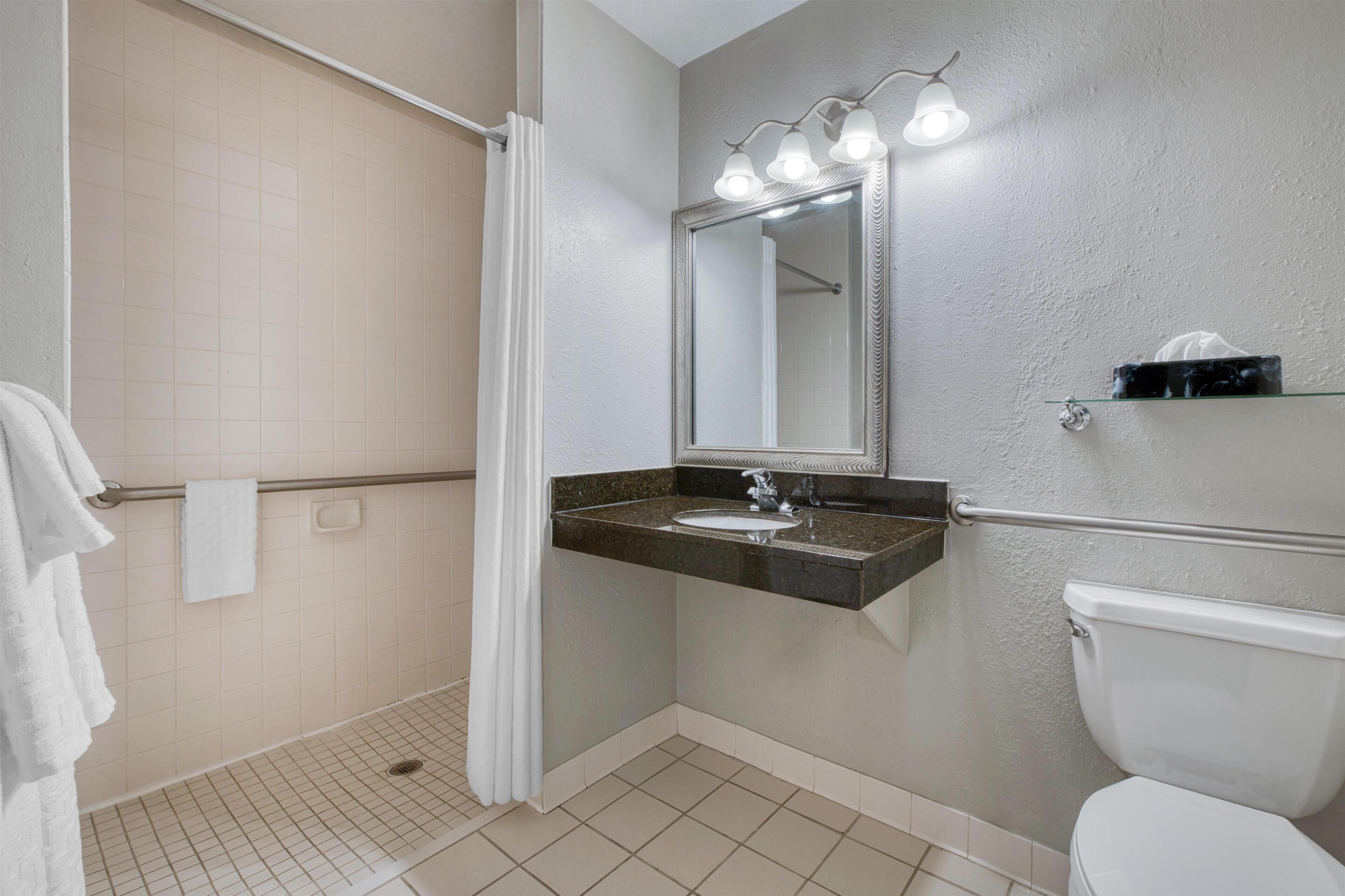 A bathroom with a shower, toilet, sink, and a mirror with lights.