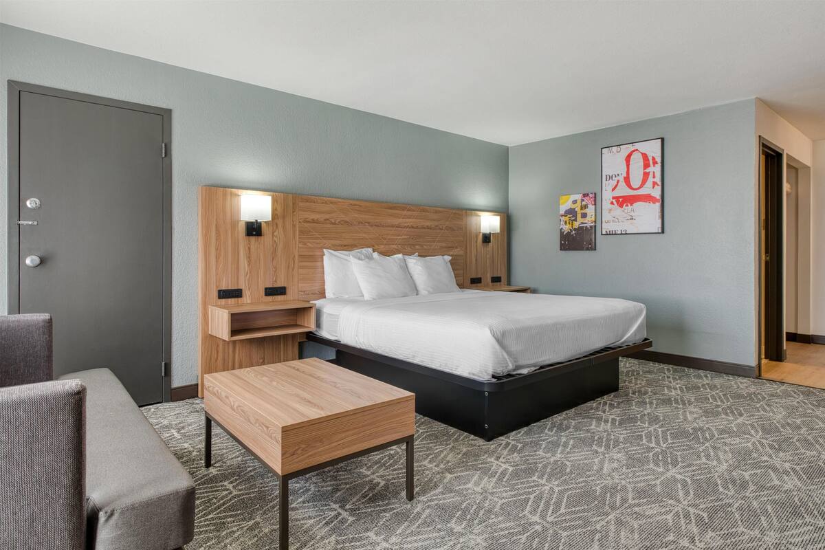 Una habitación de hotel con cama, mesitas de noche, una silla y una pequeña mesa.