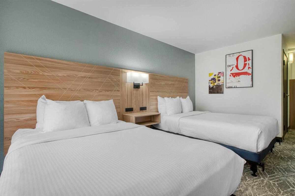 Habitación de hotel con dos camas, cabecero de madera, mesita de noche, lámpara de pared y un cartel.