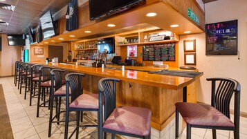 Una zona de bar con una barra larga, varios taburetes y un panel con las ofertas del día.